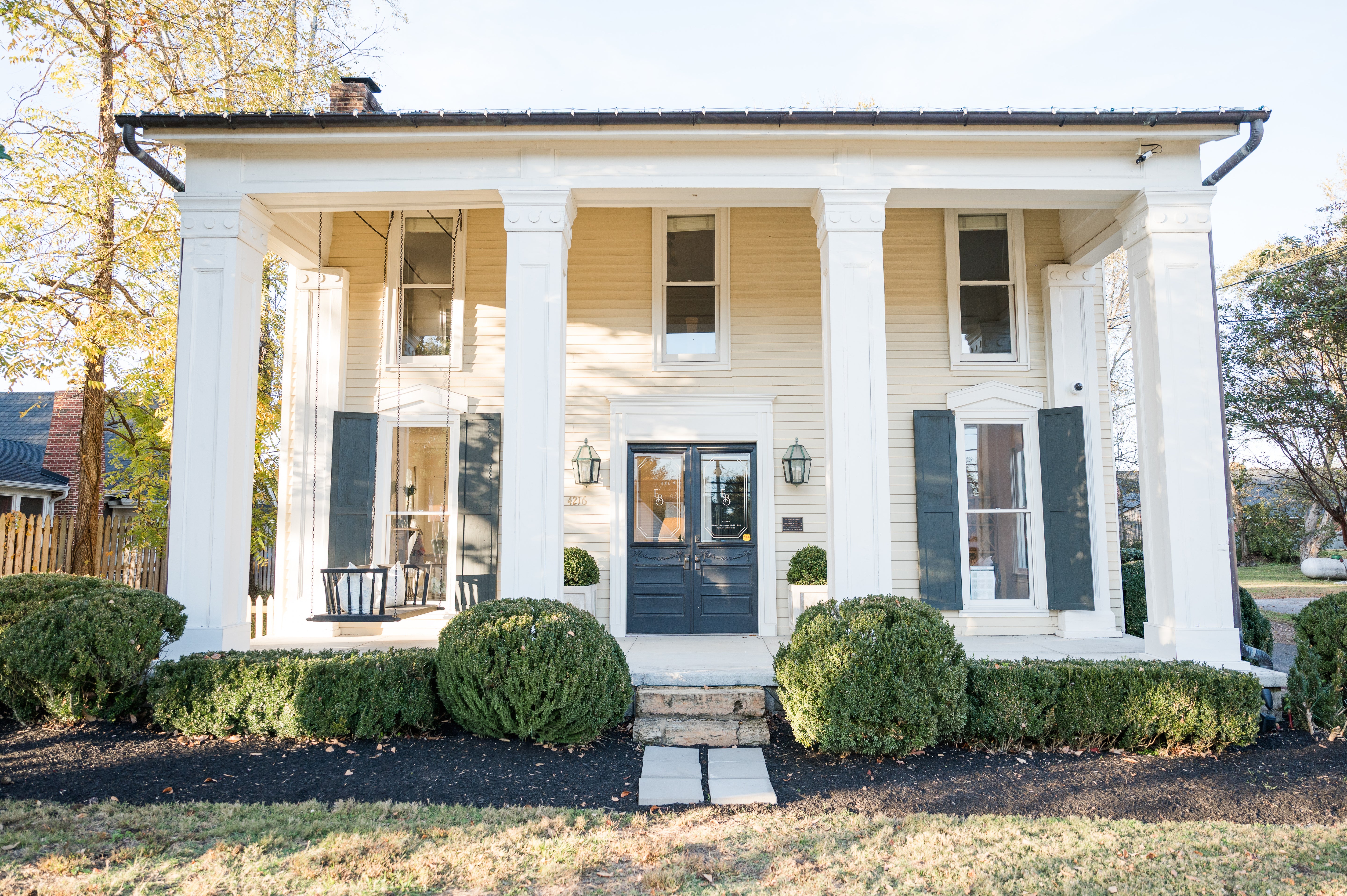 Two-story house with white columns and blue shutters on a sunny day.