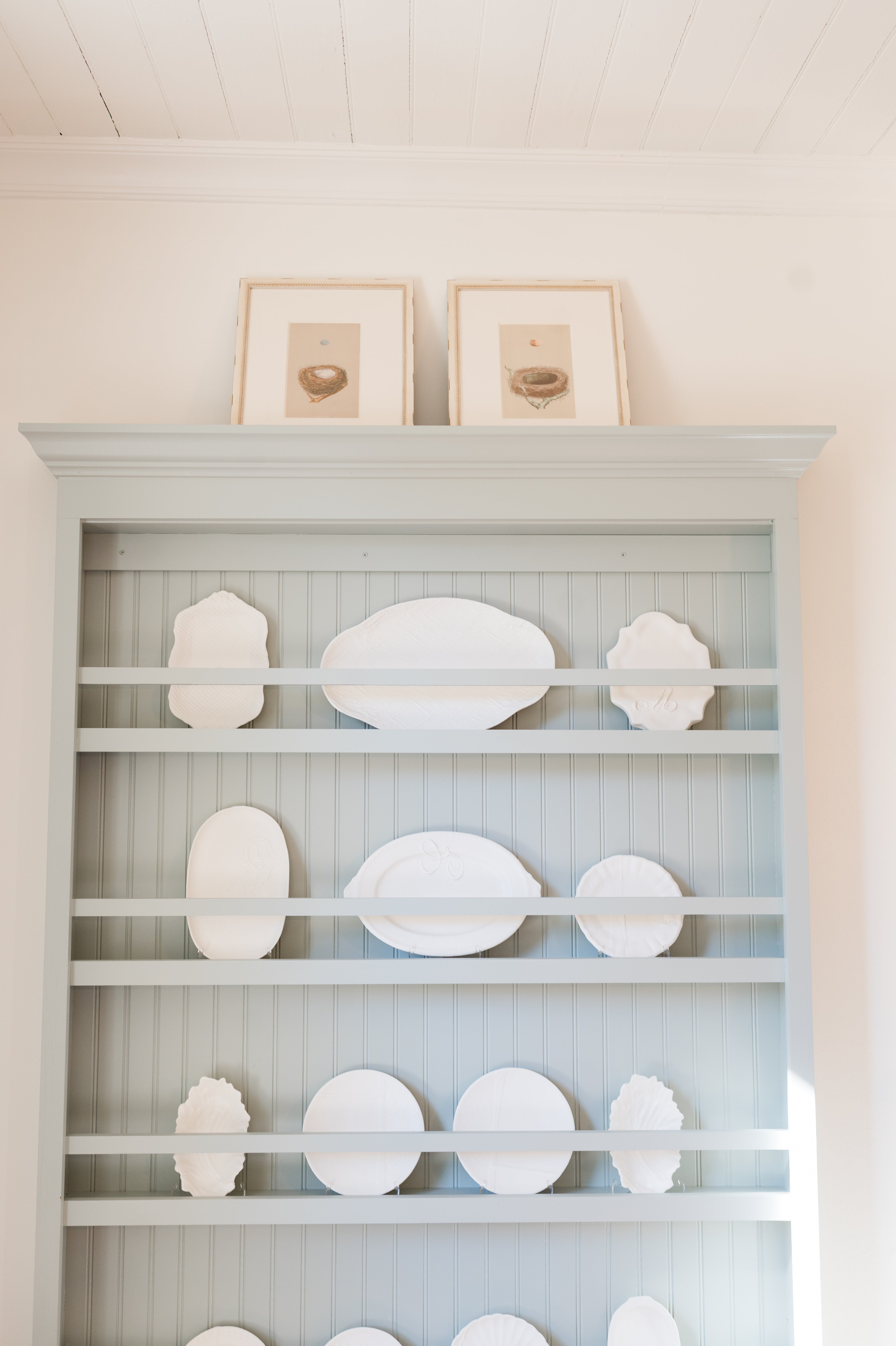 Light blue shelf with decorative white plates against a white wall