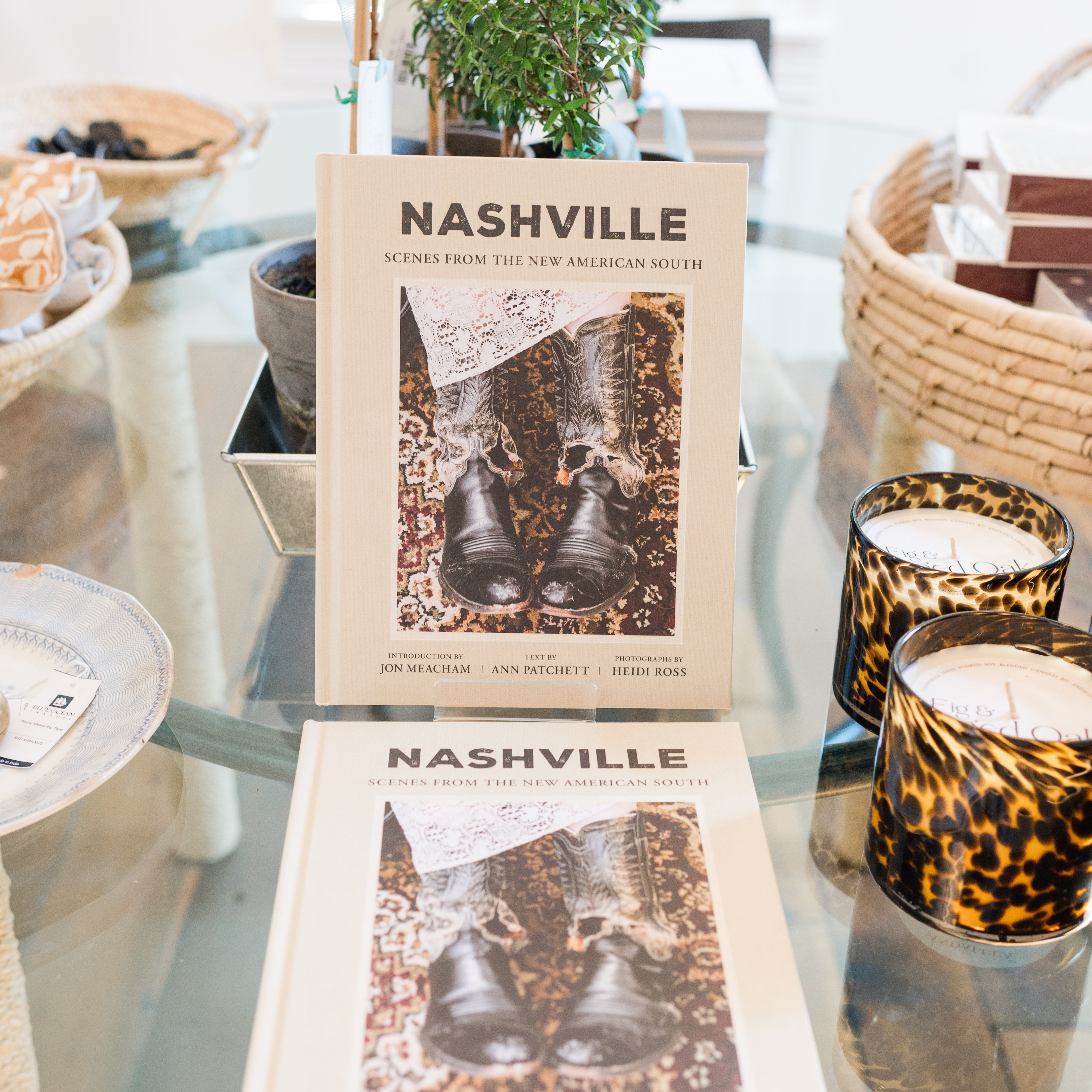 Two books titled 'Nashville' on a glass table with candles and plants in the background.