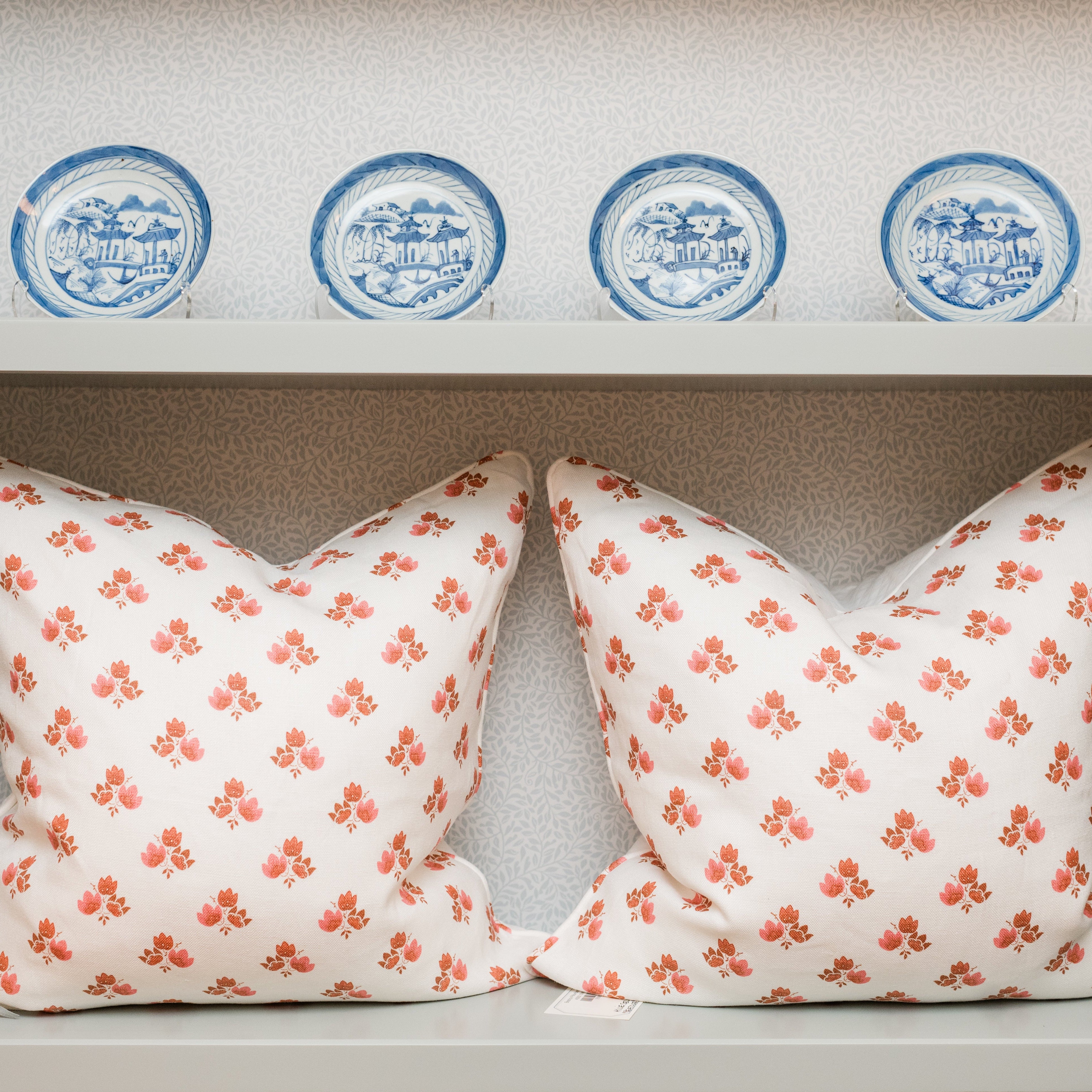 Two floral-patterned pillows on a shelf with decorative plates above.