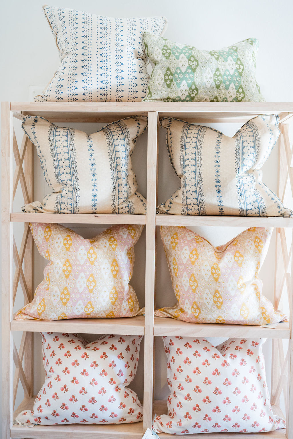 Decorative pillows with various patterns on a wooden shelf.