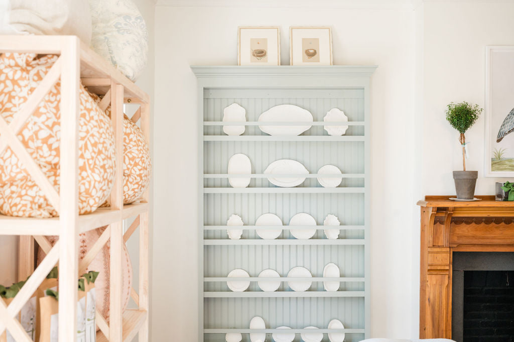 Shelving unit with decorative plates in a room with a fireplace and wooden shelf.
