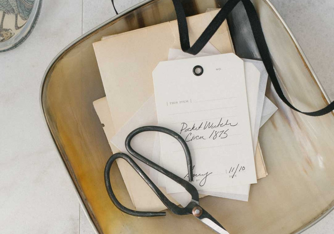 Scissors and vintage-style cards on a metallic tray with a neutral background